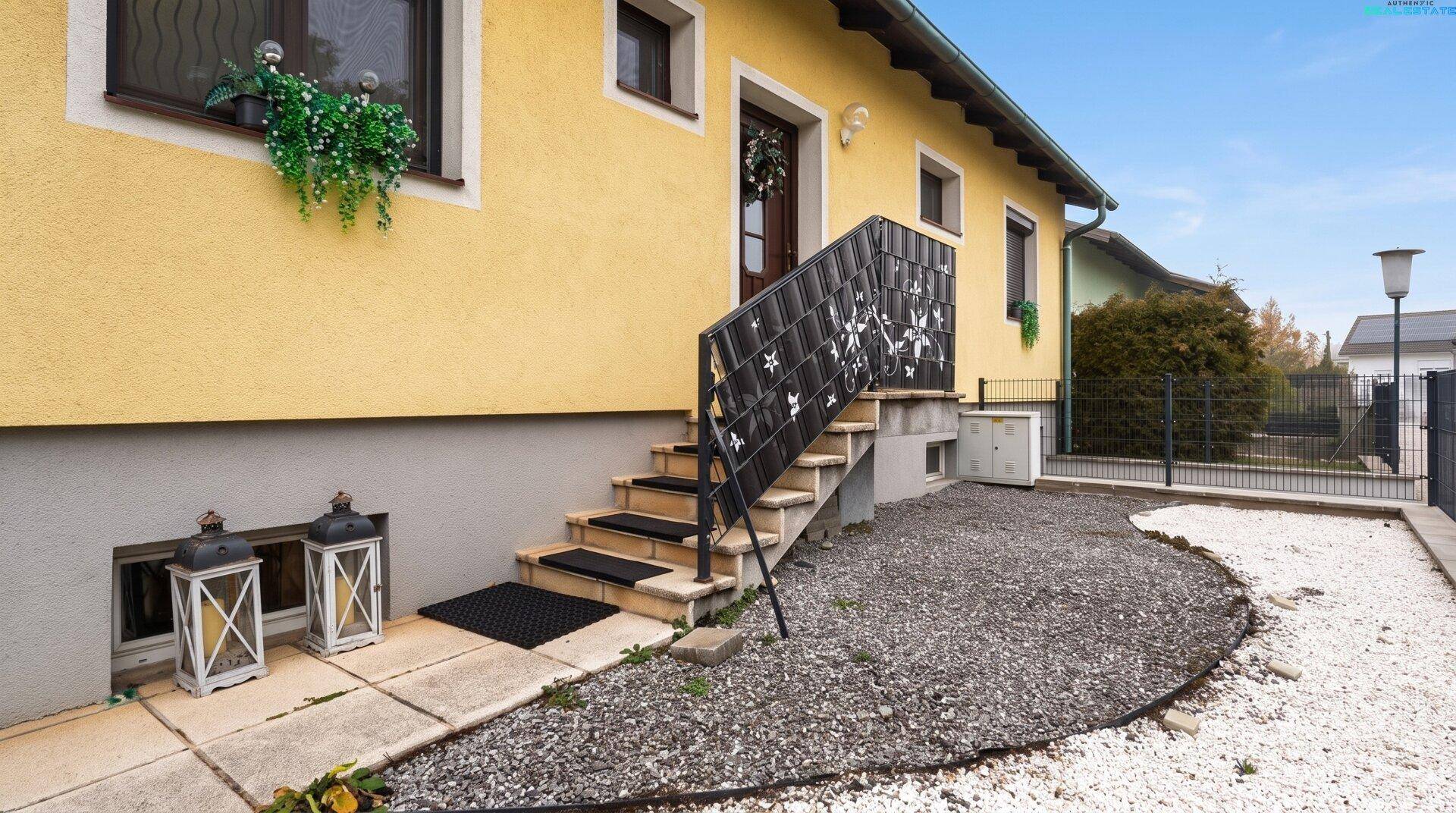 Eingangsbereich des Hauses mit Außentreppe, schmiedeeisernem Geländer und Kiesbeet.