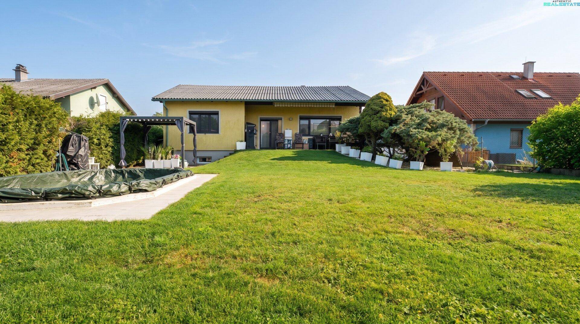 Weitläufiger Gartenbereich mit grüner Rasenfläche, Poolabdeckung und der Rückseite des Hauses.