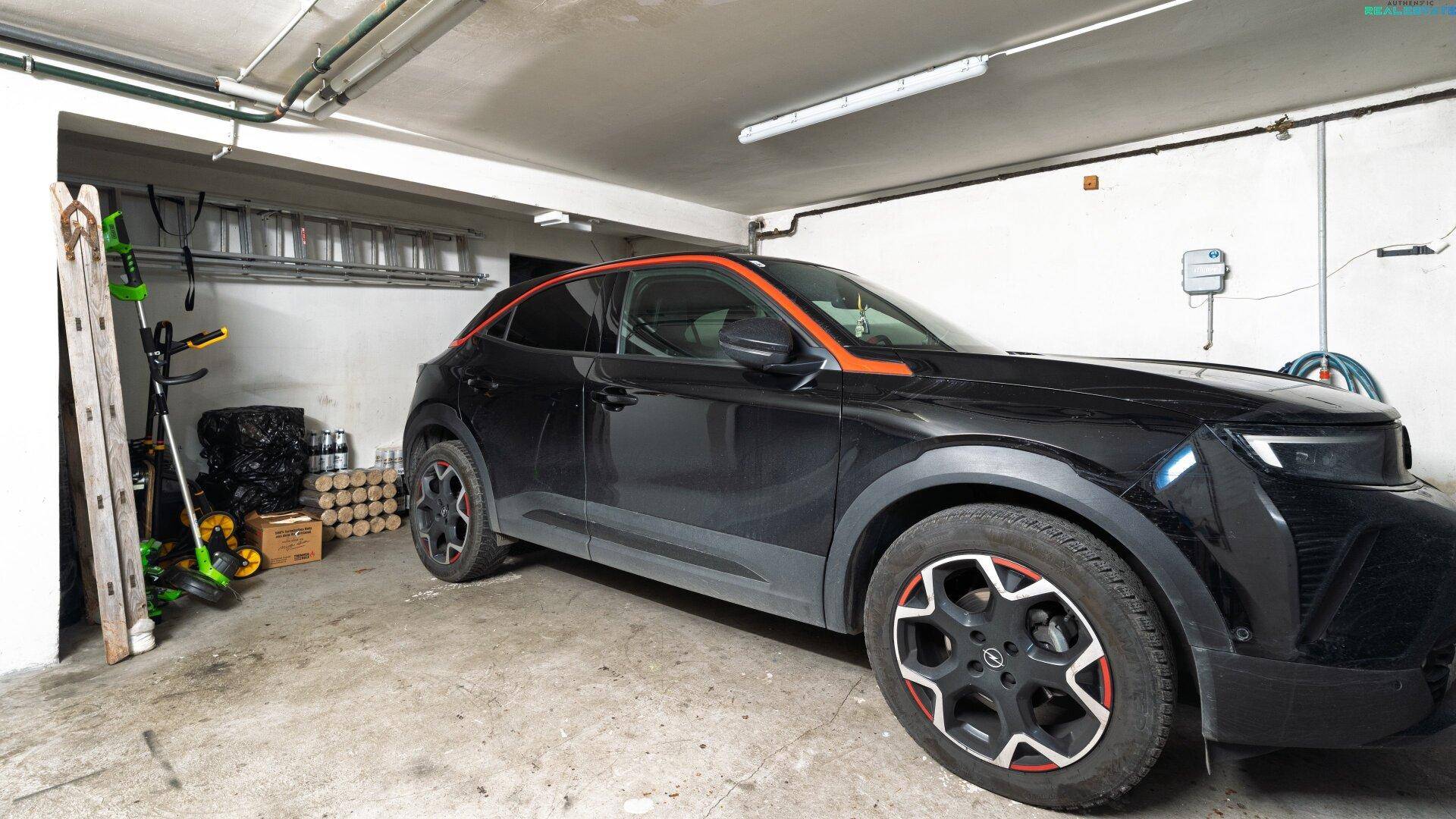 Geräumige Garage mit einem geparkten Auto und Stauraum für Gartengeräte.
