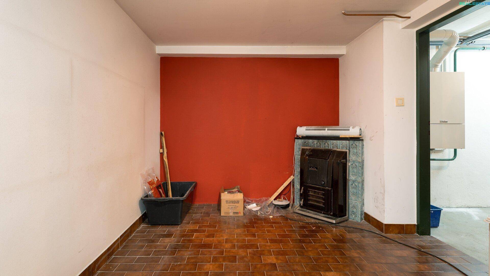 Kellerraum mit roter Akzentwand, Fliesenboden und einem Holzofen für zusätzliche Wärme.