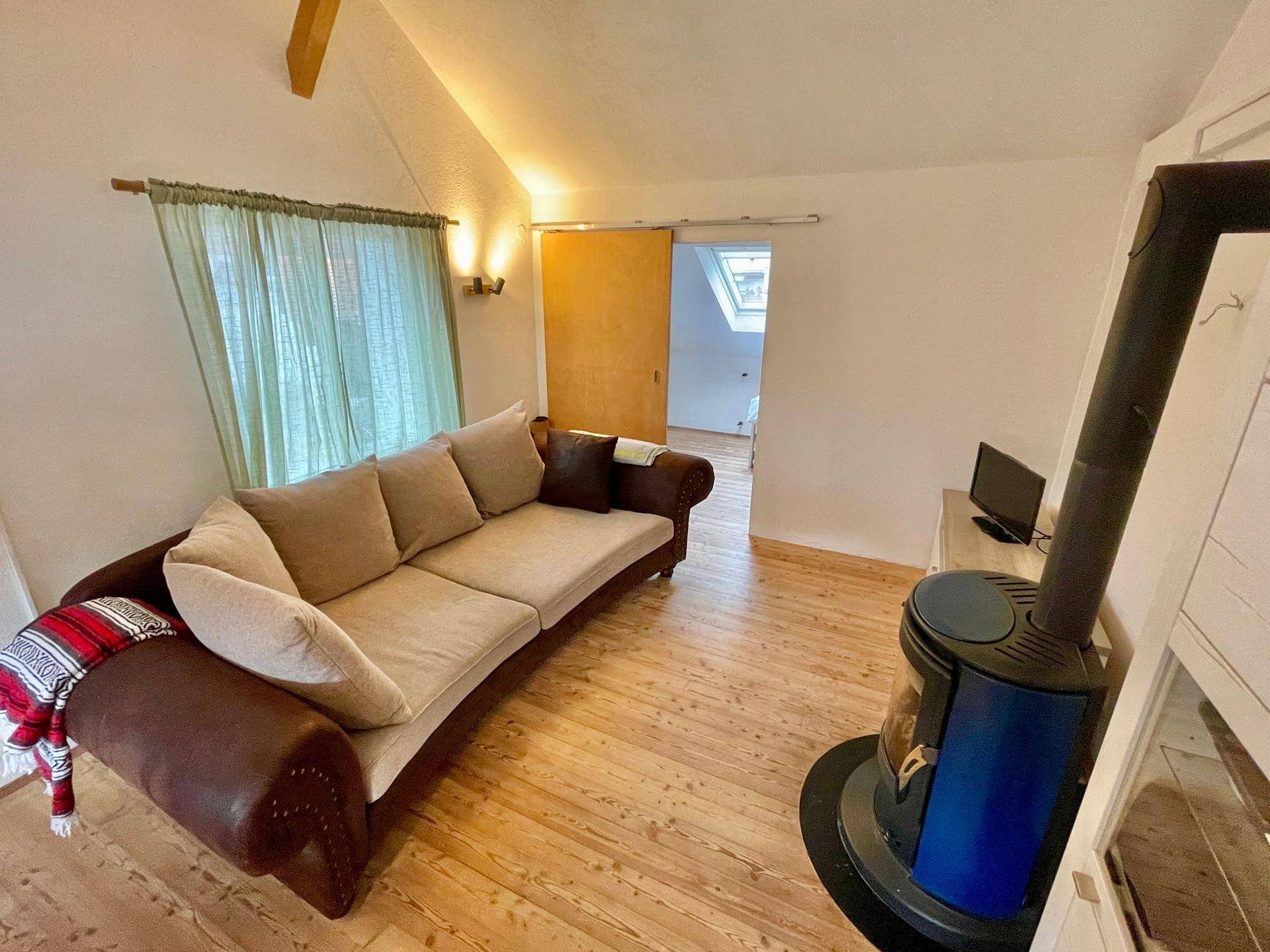 Wohnzimmer mit großem Sofa, Kaminofen und Zugang zu einem weiteren Raum.