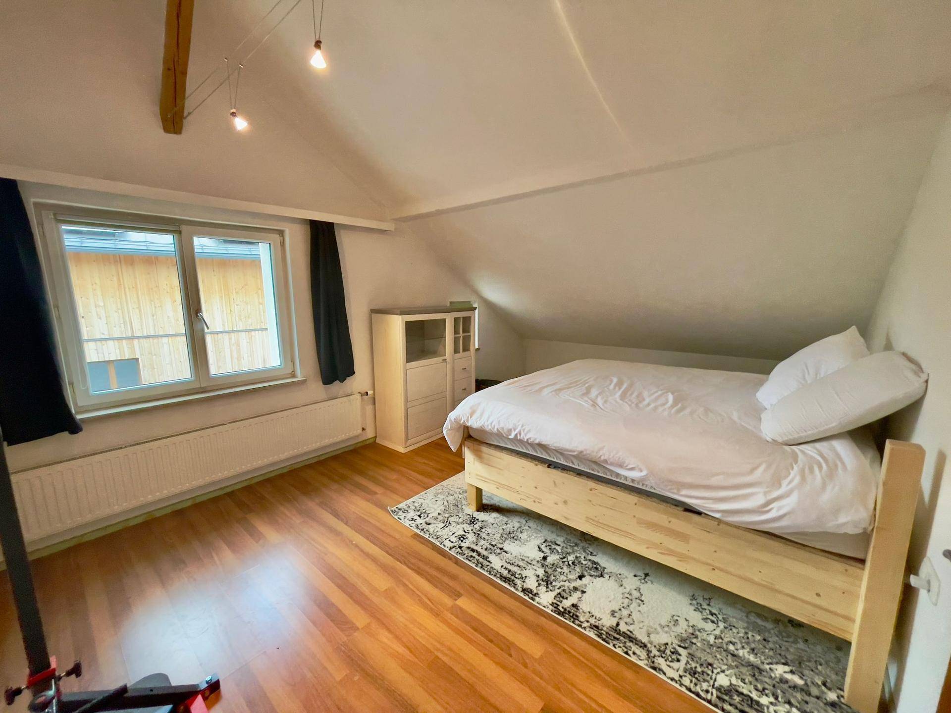 Schlafzimmer mit Holzboden, Bett, Fenster und Dachschräge.