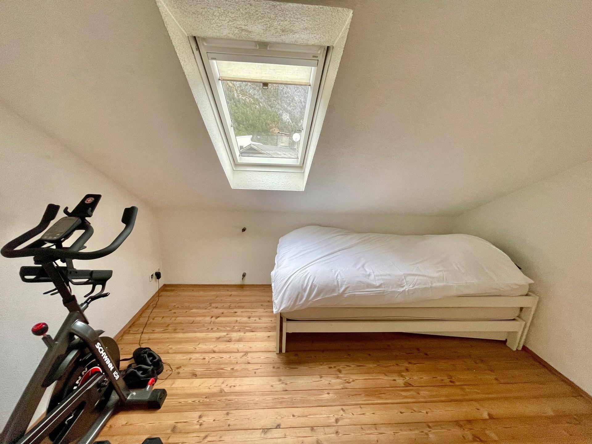 Schlafzimmer im Dachgeschoss mit Holzboden, Dachfenster und Fitnessgerät.