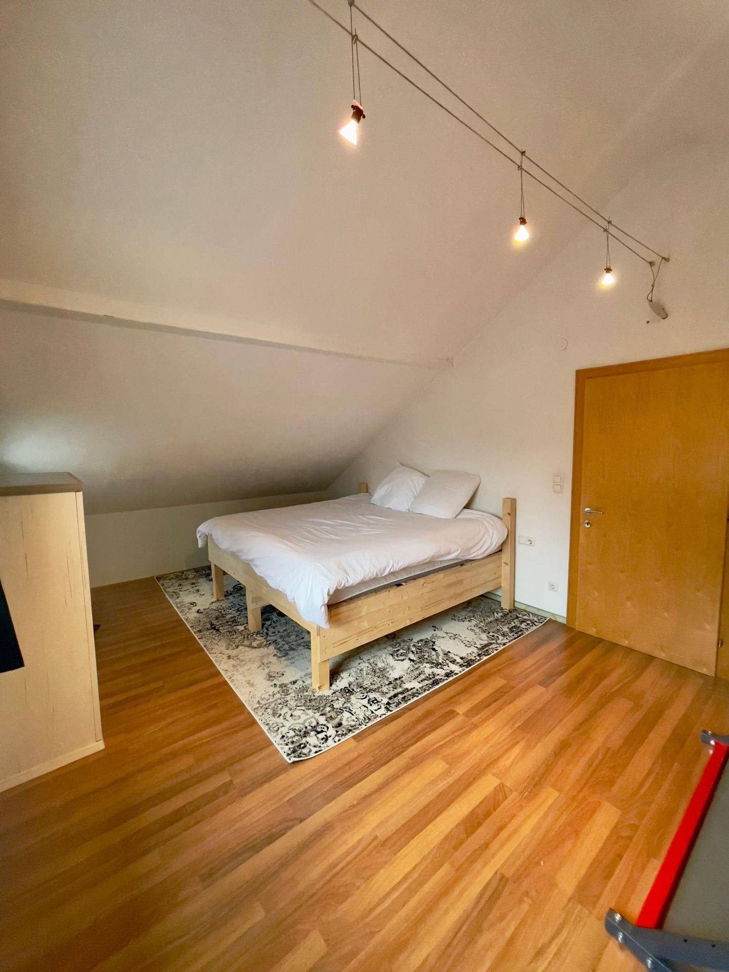 Schlafzimmer mit Holzboden, Doppelbett und schrägen Wänden im Dachgeschoss.