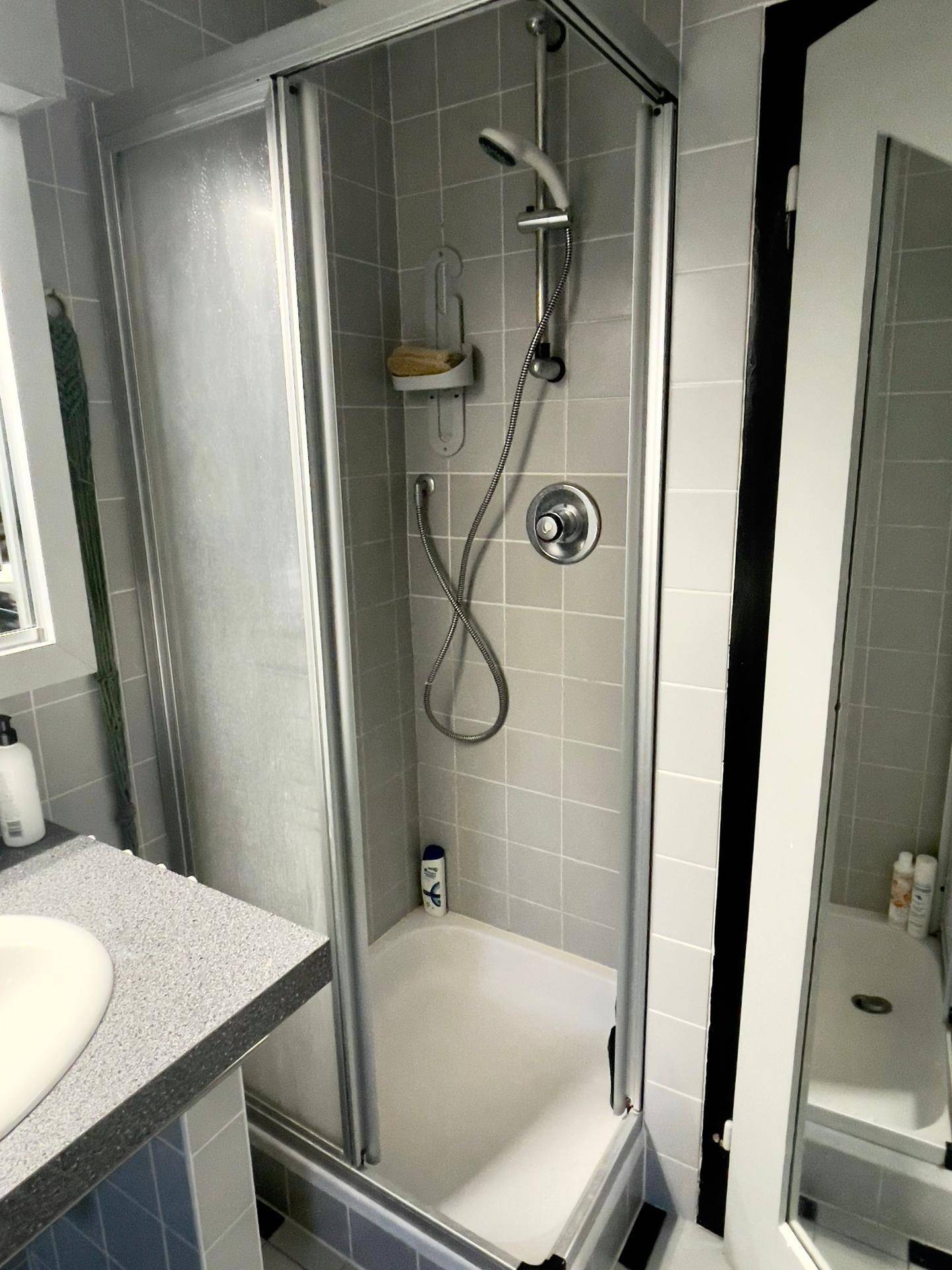 Duschbereich im Badezimmer mit grauen Fliesen und Duschkabine.