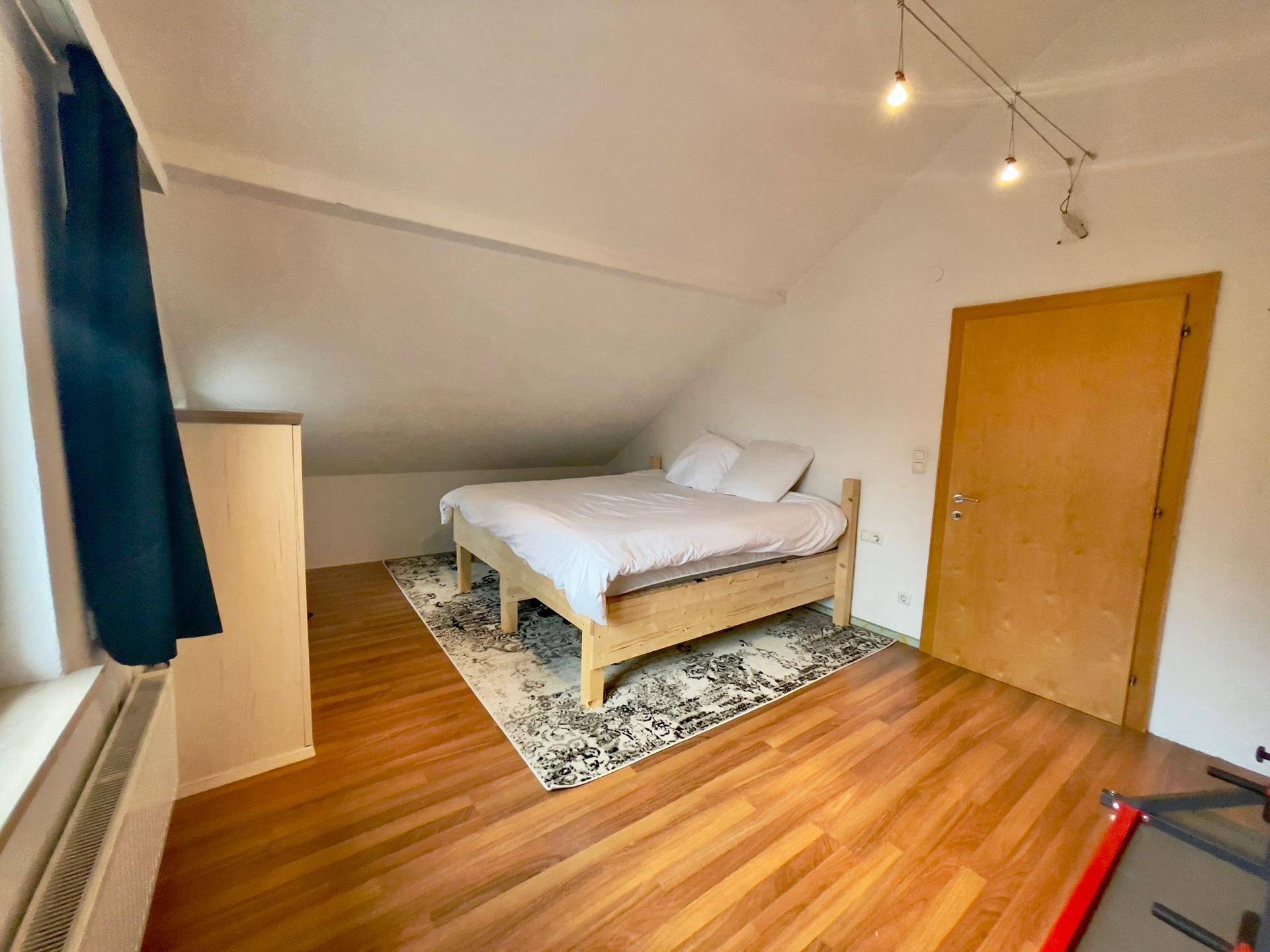 Helles Schlafzimmer im Dachgeschoss mit Holzboden, Bett und Dachschräge.