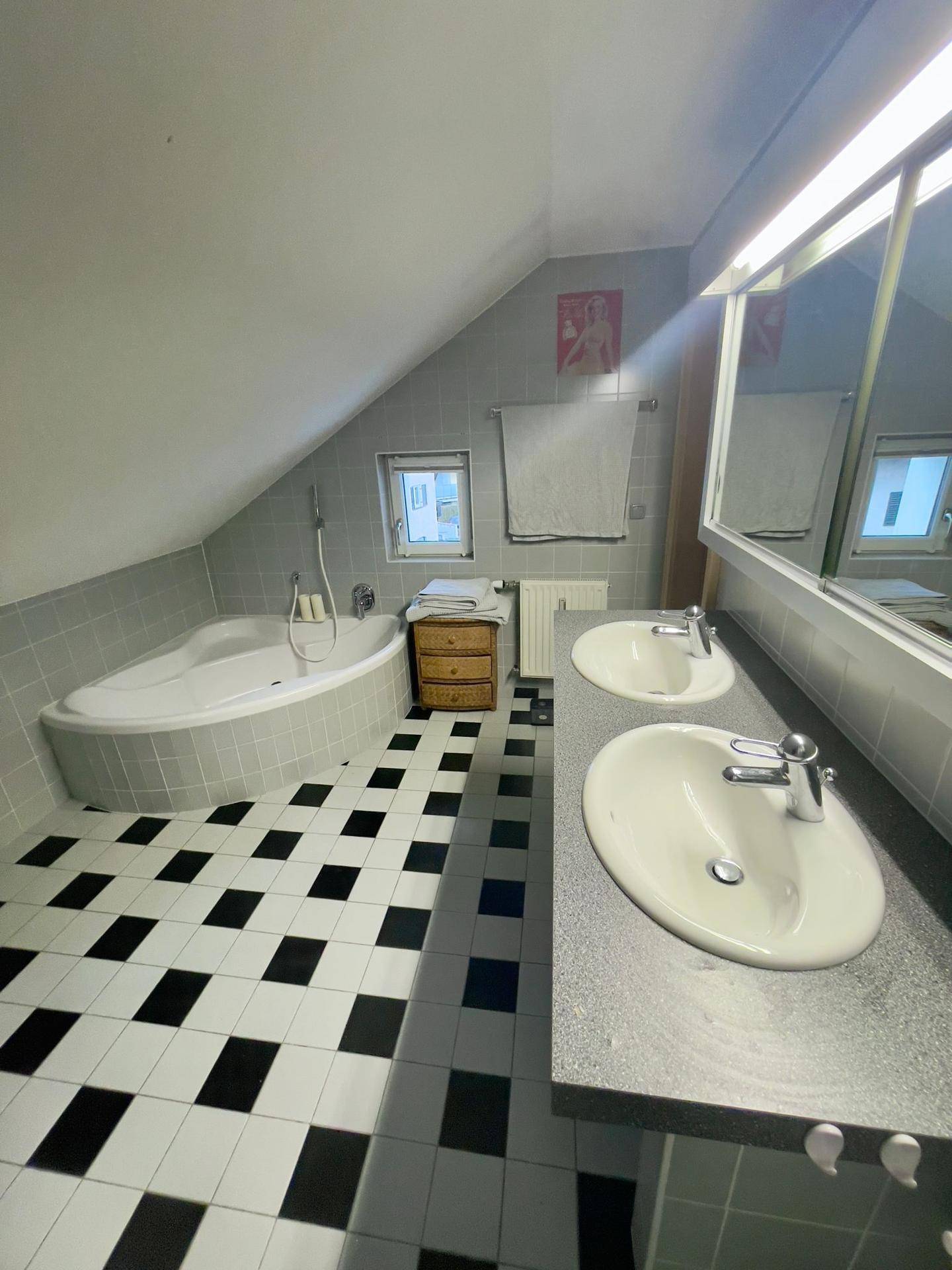 Badezimmer mit Doppelwaschbecken, Badewanne und schwarz-weißem Fliesenboden.