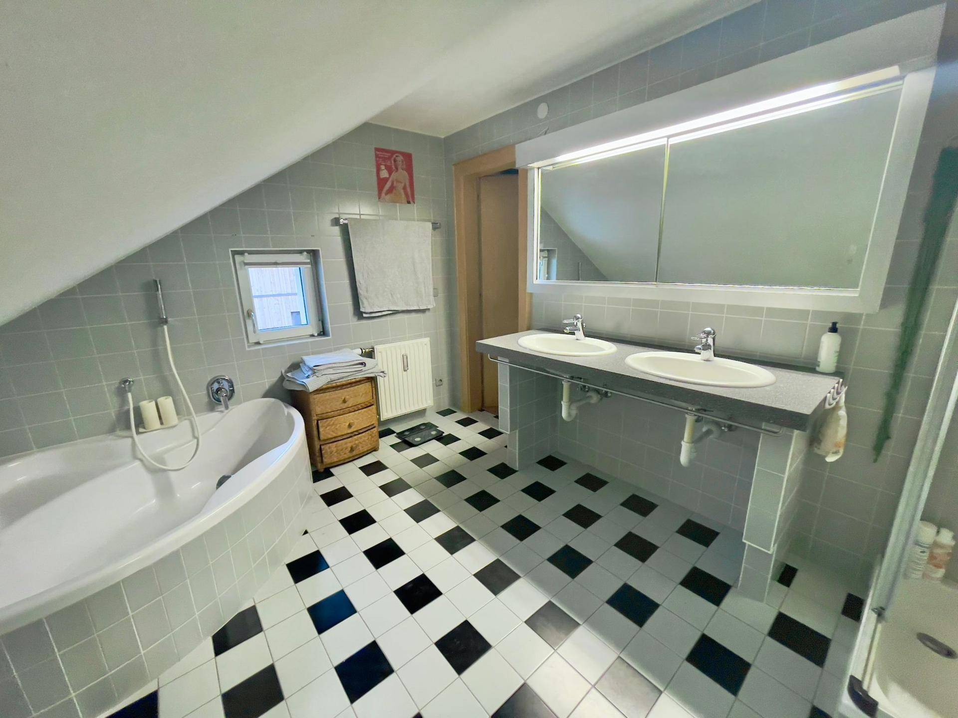 Geräumiges Badezimmer mit Doppelwaschbecken, Badewanne und schwarz-weißem Fliesenboden.