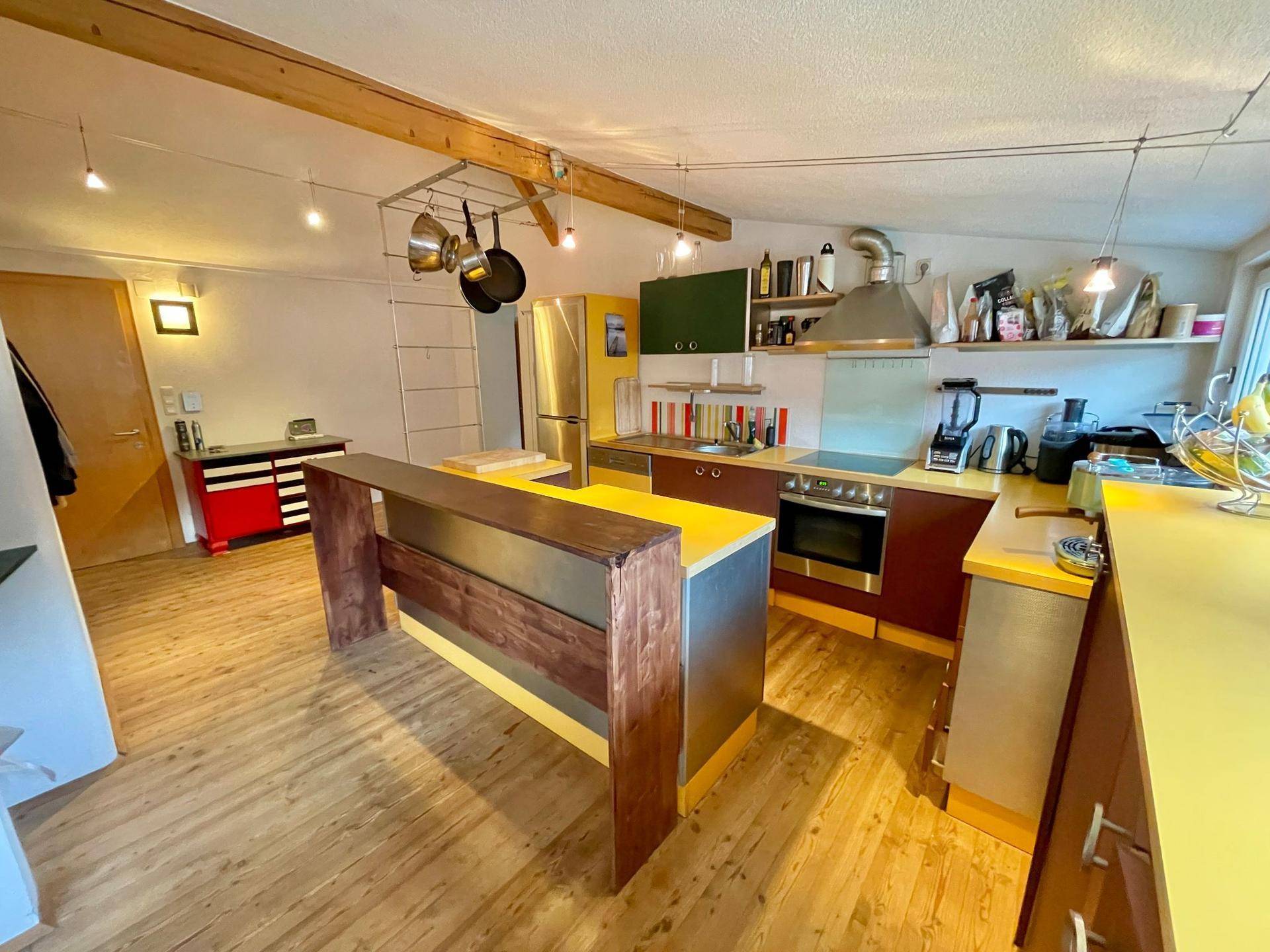 Geräumige Küche mit gelben Arbeitsplatten, Holzboden und Blick auf den Flur.