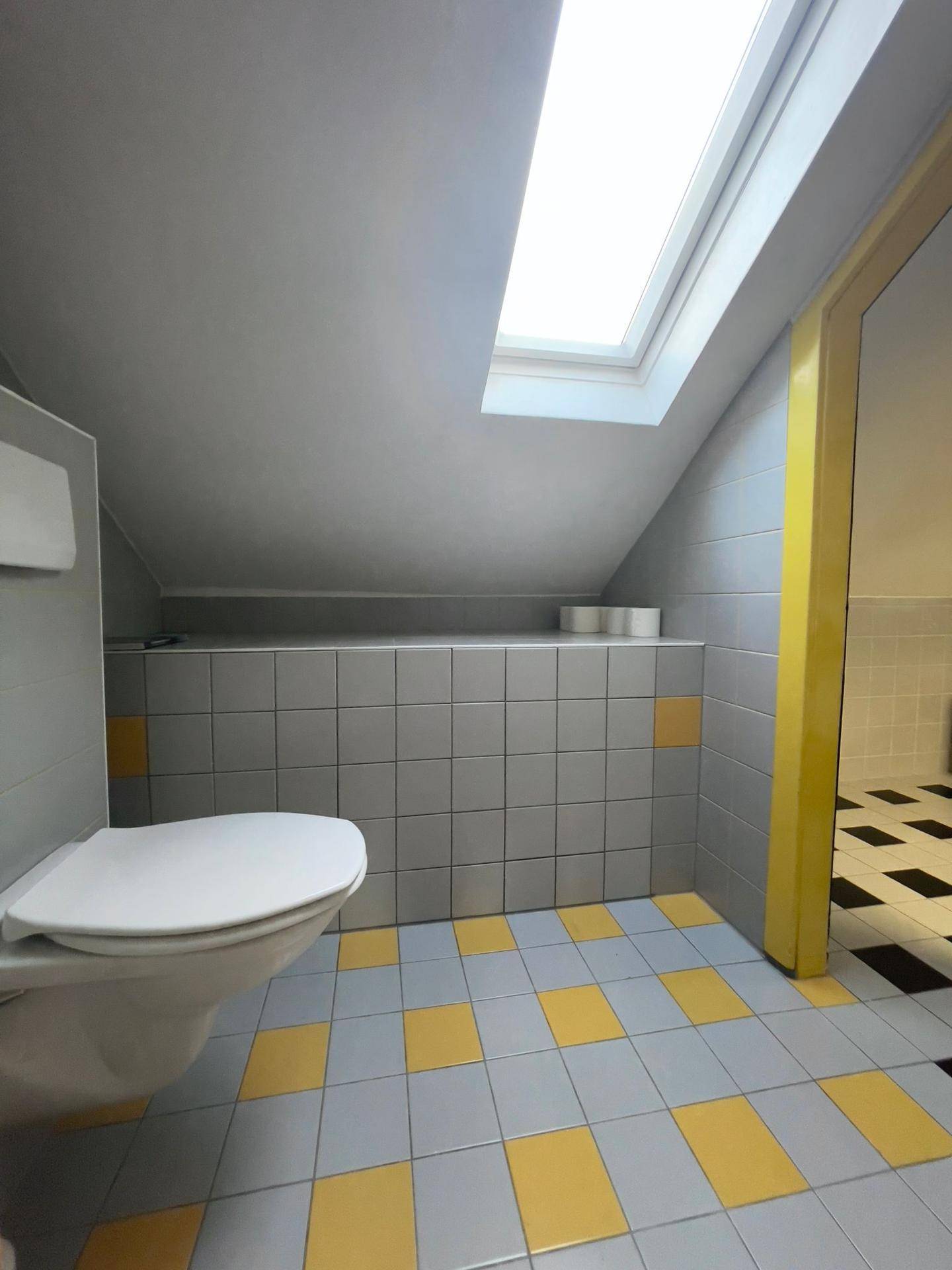 Separate Toilette mit Dachfenster und gelb-grau kariertem Fliesenboden.