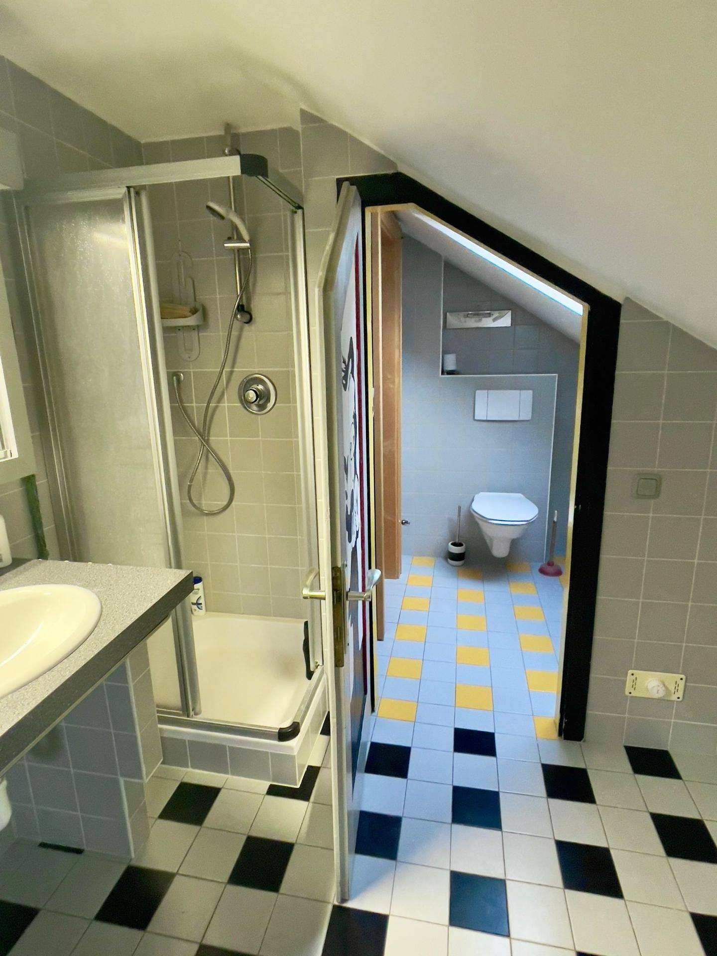Badezimmer mit Dusche, WC und auffälligen schwarz-gelb-grauen Fliesen.