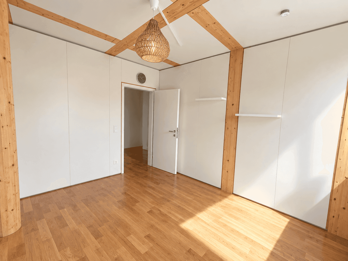 Geräumiges Zimmer mit Holzboden, Deckenbalken und einem dekorativen Deckenventilator.