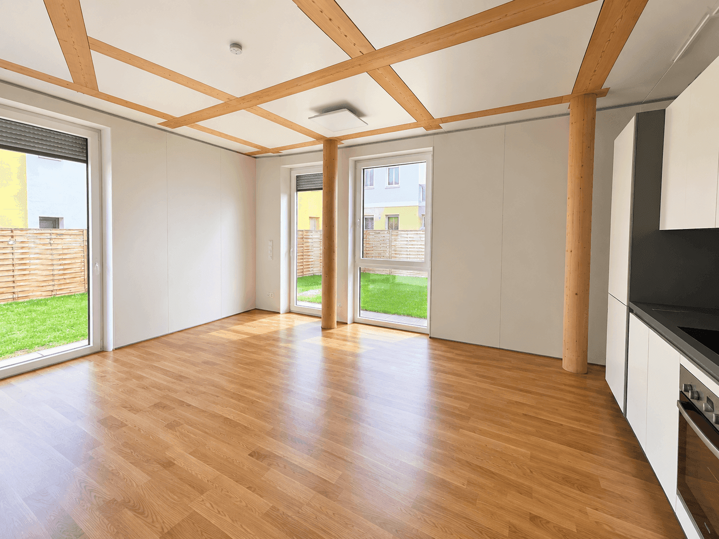 Offener Wohnbereich mit integrierter Küchenzeile, Holzbalkendecke und direktem Gartenzugang.