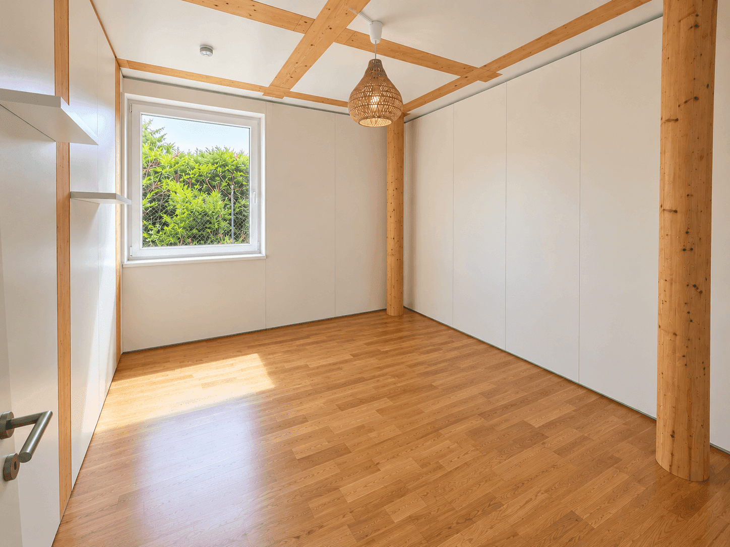 Helles Zimmer mit Eichenparkett, Deckenbalken und einem Fenster mit Blick ins Grüne.