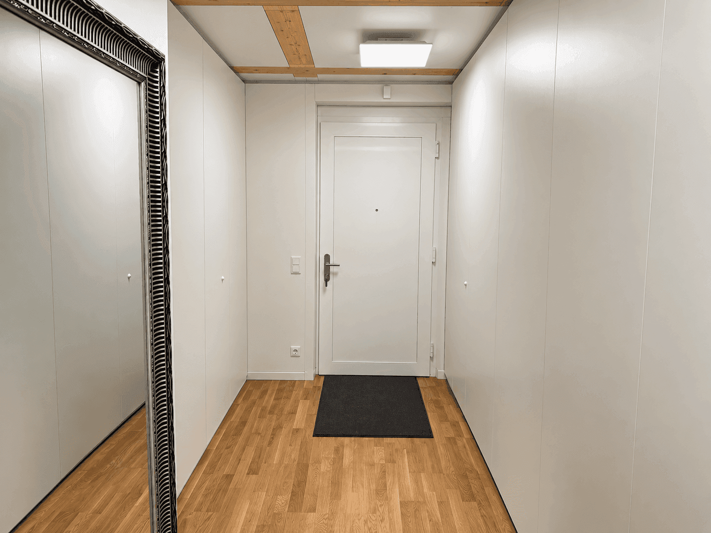 Eingangsbereich mit Holzboden, weißer Wandverkleidung und einem großen Wandspiegel.