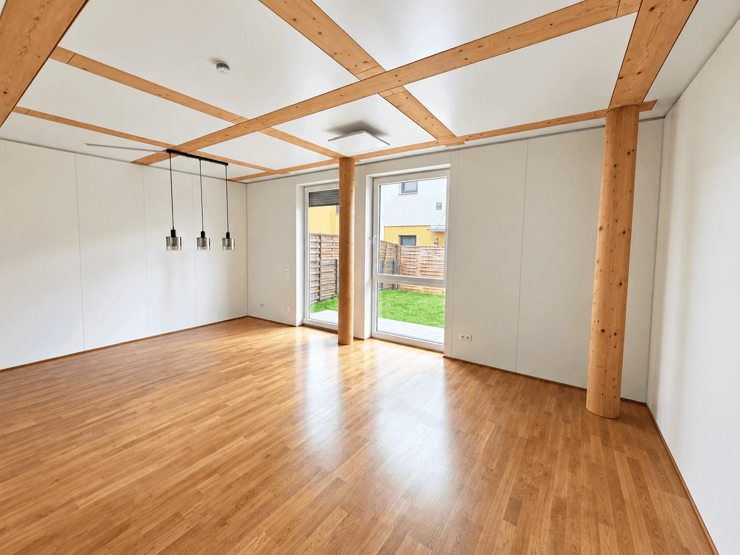 Heller Wohnraum mit Eichenparkett, sichtbaren Holzdeckenbalken und Zugang zum Garten.
