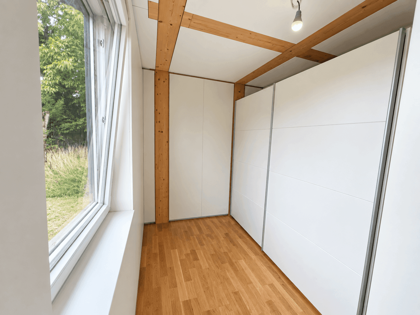 Helles Schlafzimmer mit Eichenparkett, Einbauschränken und Blick ins Grüne.