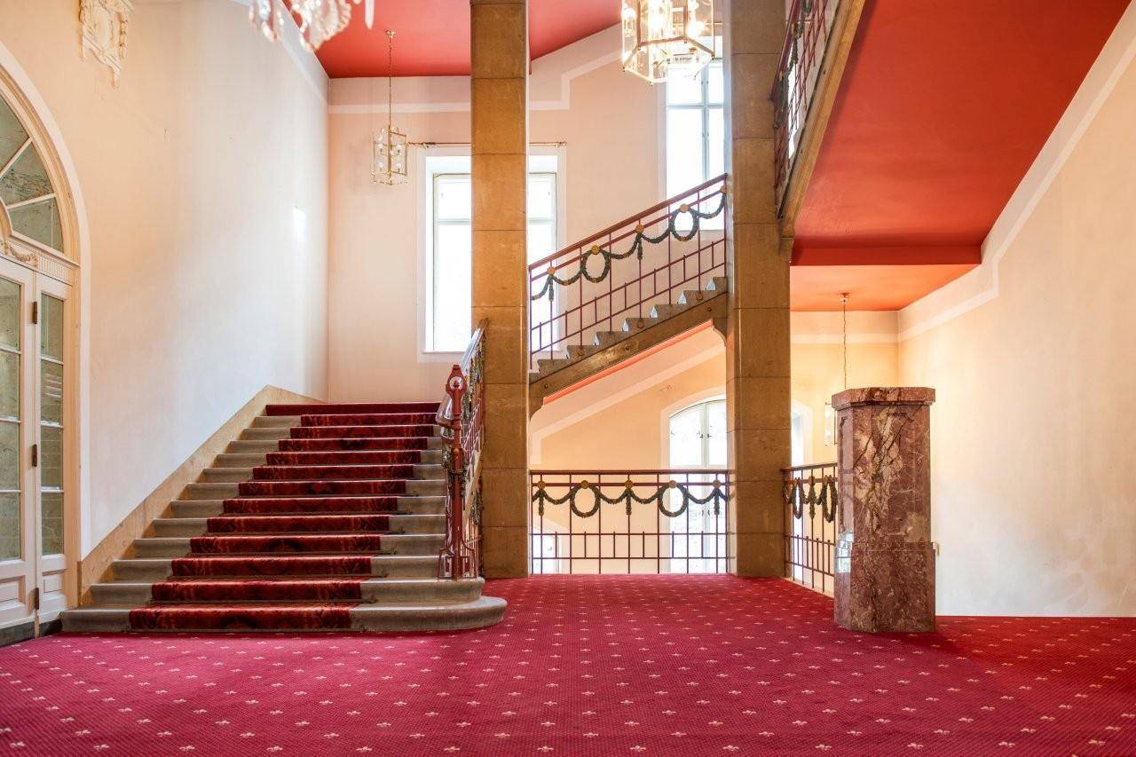Prunkvolles Treppenhaus mit rotem Teppich, verzierten Geländern und hohen Decken.