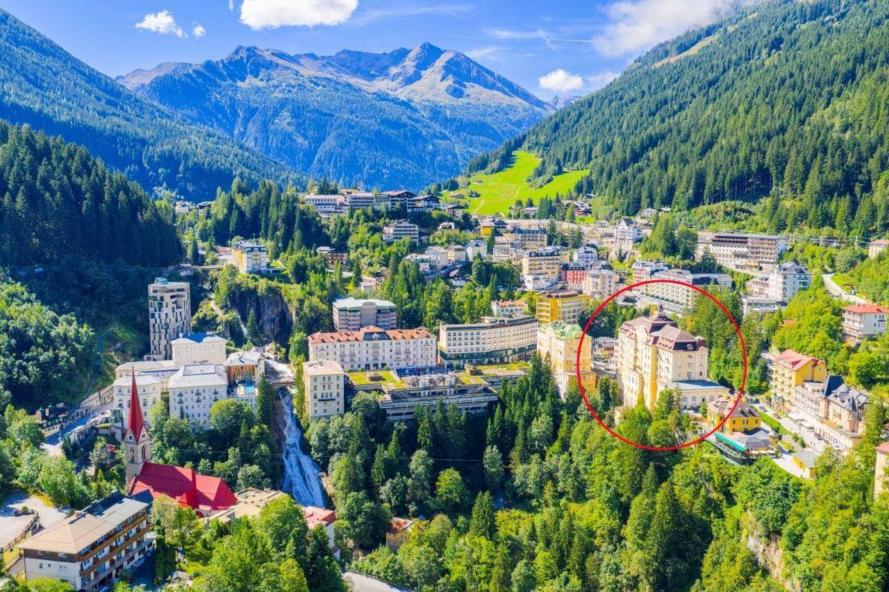 Luftaufnahme einer malerischen Stadt in einem Tal, umgeben von Bergen, mit einem markierten Gebäude.