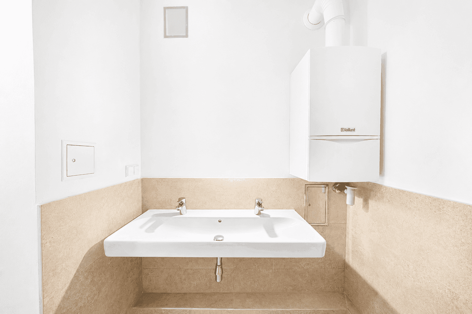 Heller Waschtisch mit zwei Armaturen und Wandfliesen in neutralem Beigeton.