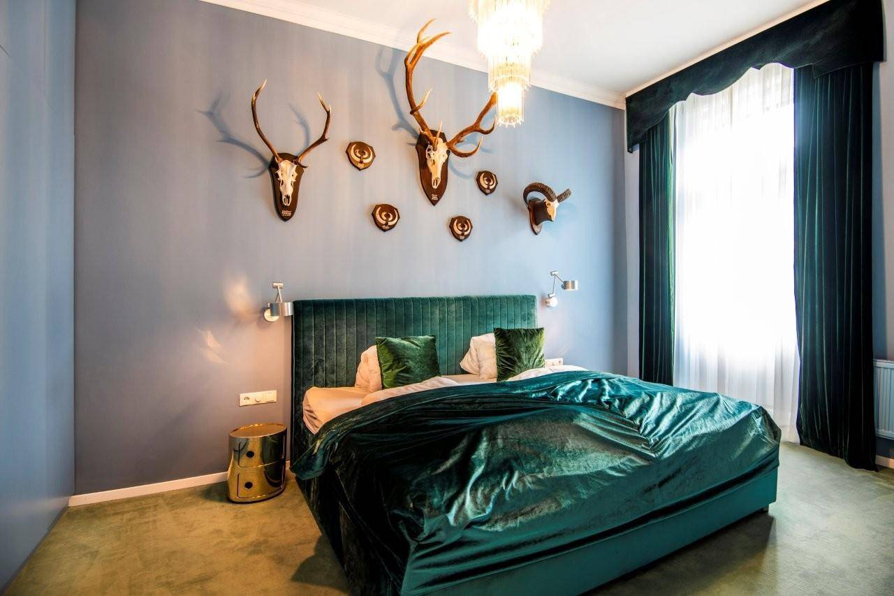 Elegantes Schlafzimmer mit großem Bett, grüner Samtdecke und Hirschgeweih-Dekoration an der Wand.