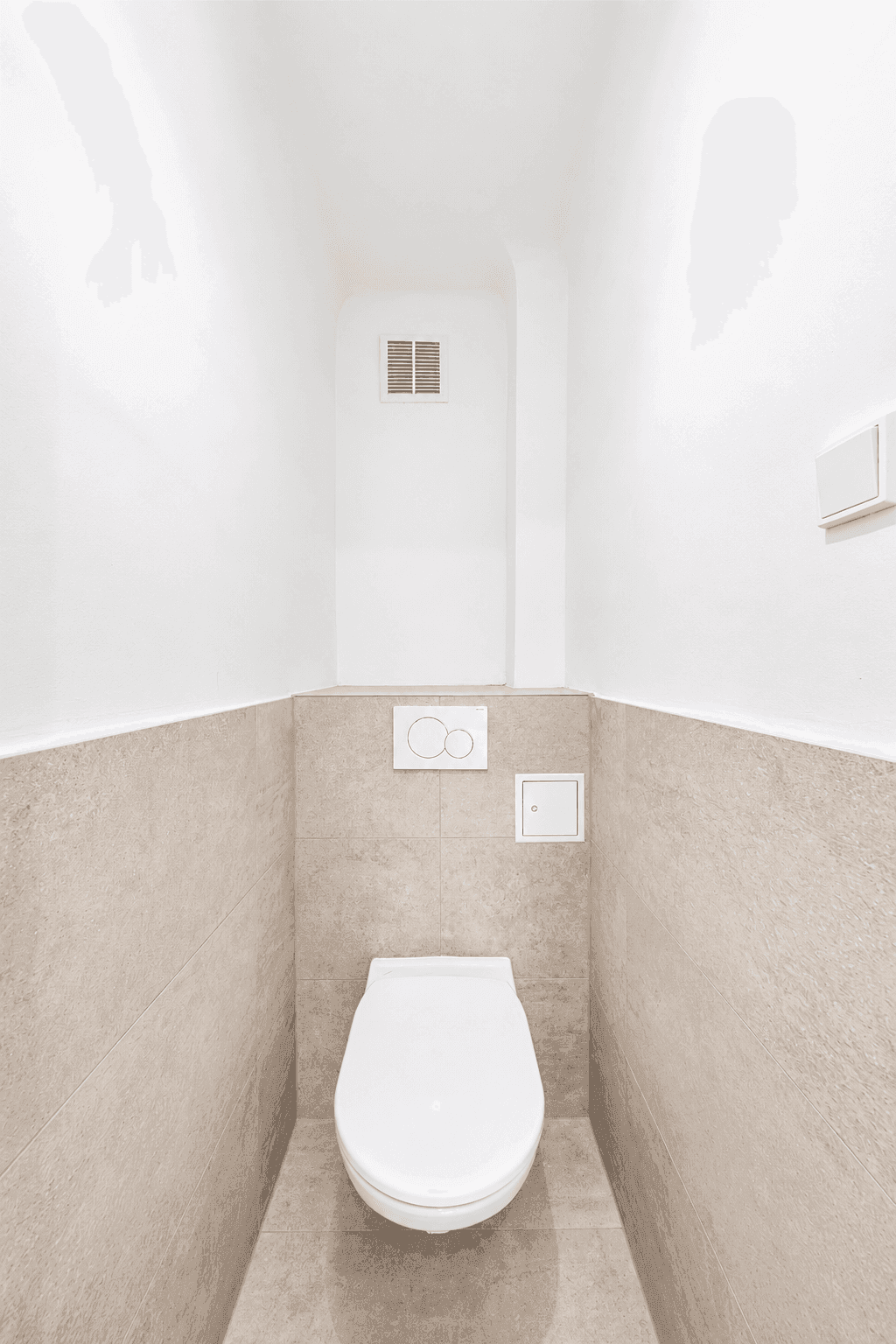Separates WC mit Wand-WC und beigefarbenen Fliesen an Wänden und Boden.