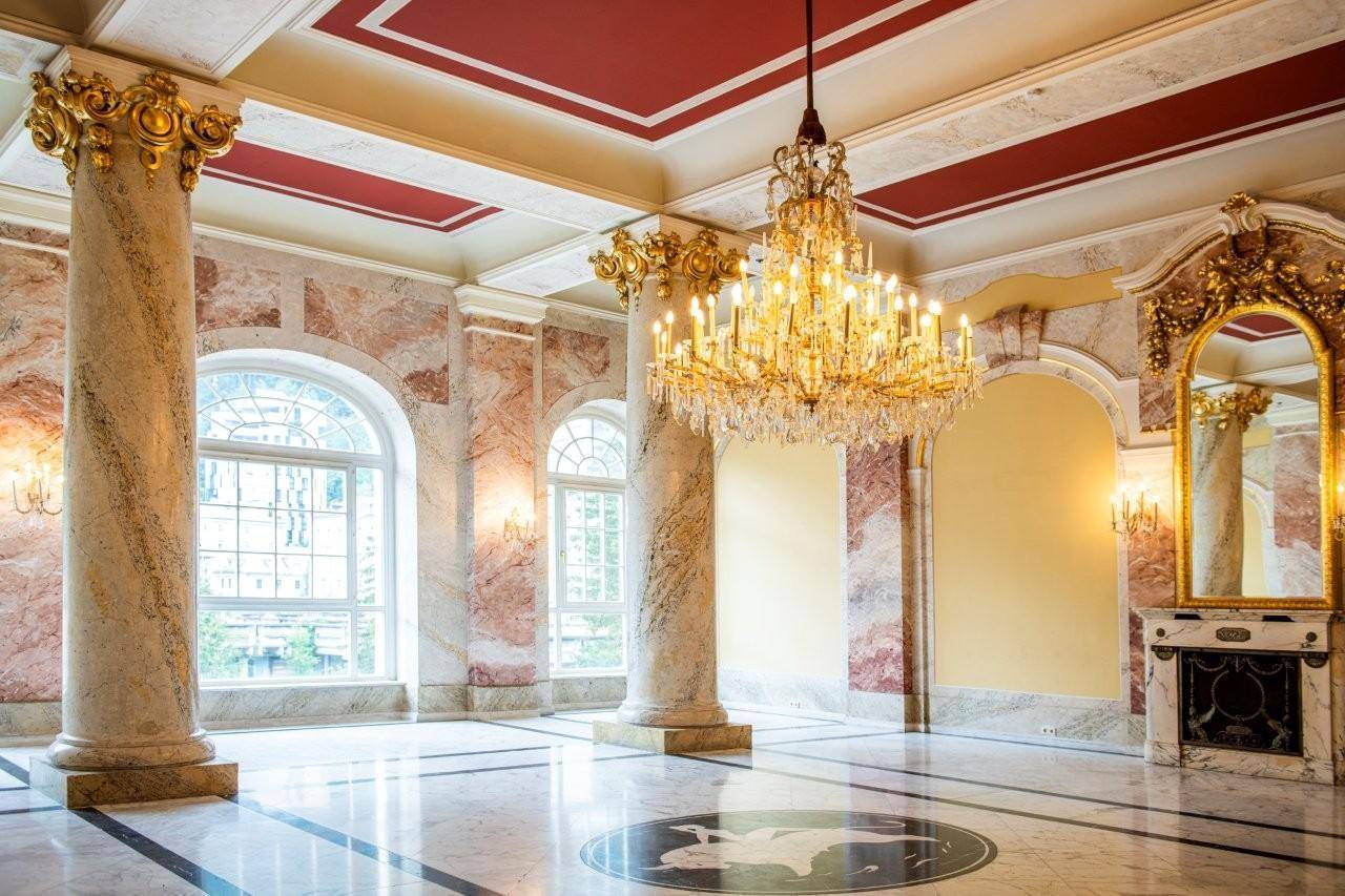 Prunkvoller Saal mit Marmorsäulen, goldenen Verzierungen und einem imposanten Kronleuchter.