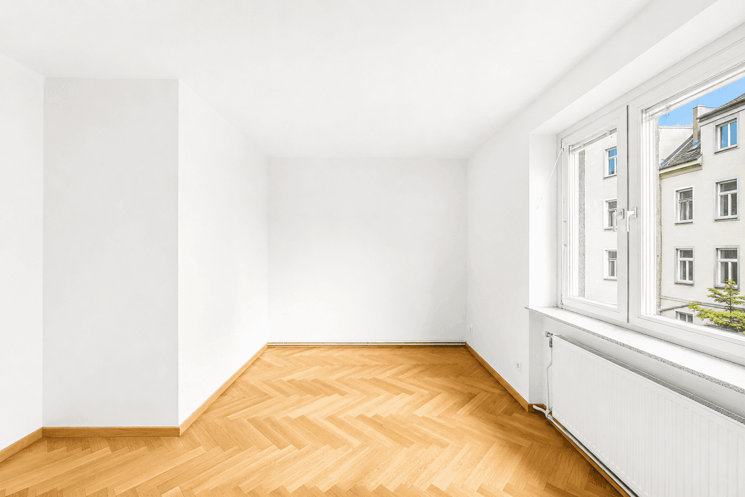 Geräumiges Zimmer mit hellem Fischgrätparkett und Blick auf die umliegenden Gebäude.