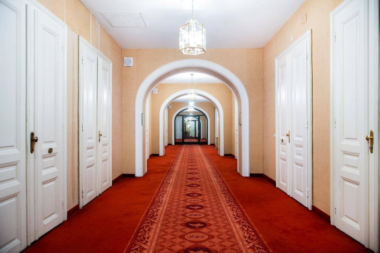 Langer, eleganter Flur mit roten Teppichläufern und mehreren gewölbten Durchgängen.