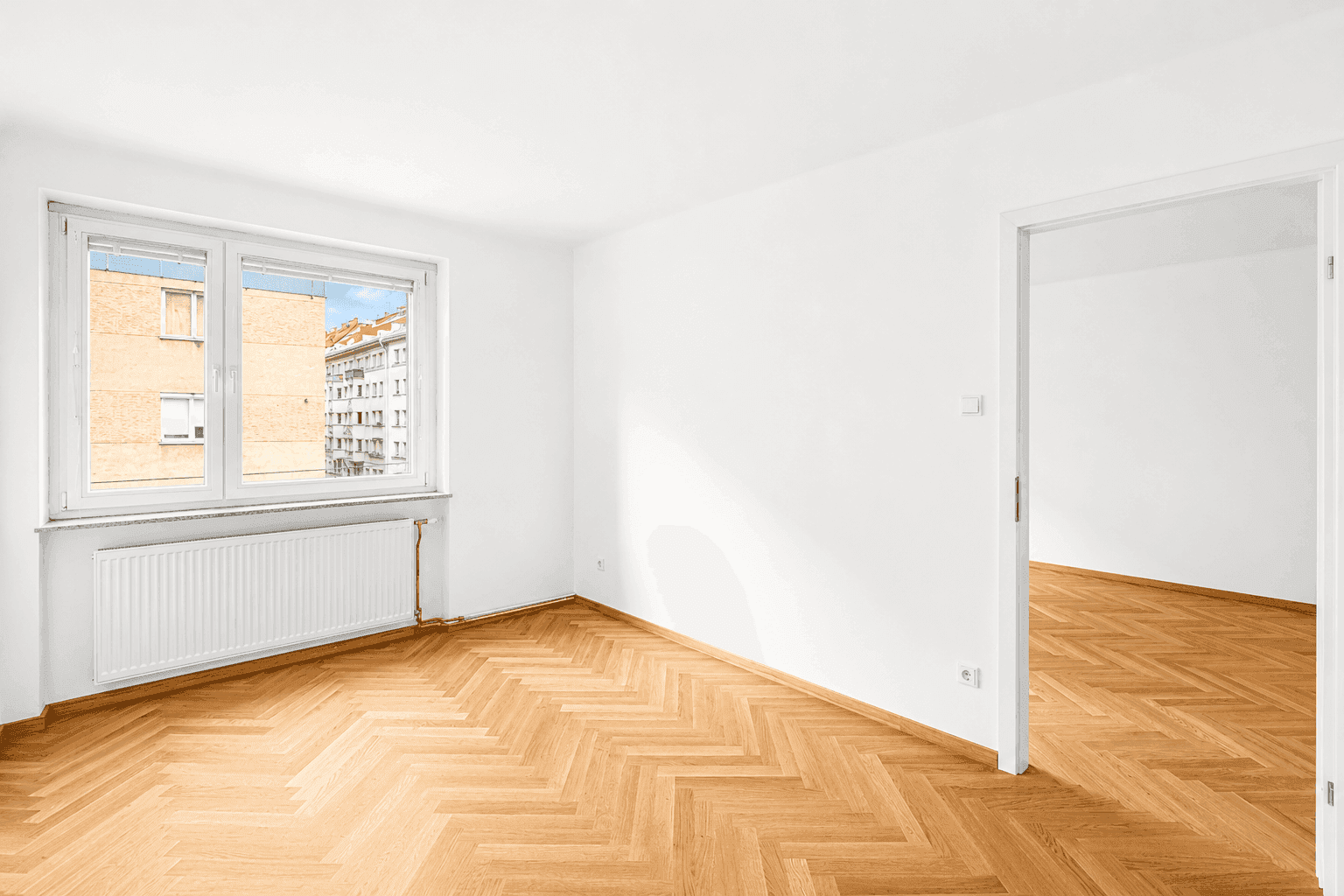 Lichtdurchfluteter Raum mit klassischem Fischgrätparkett und Heizkörper unter dem Fenster.