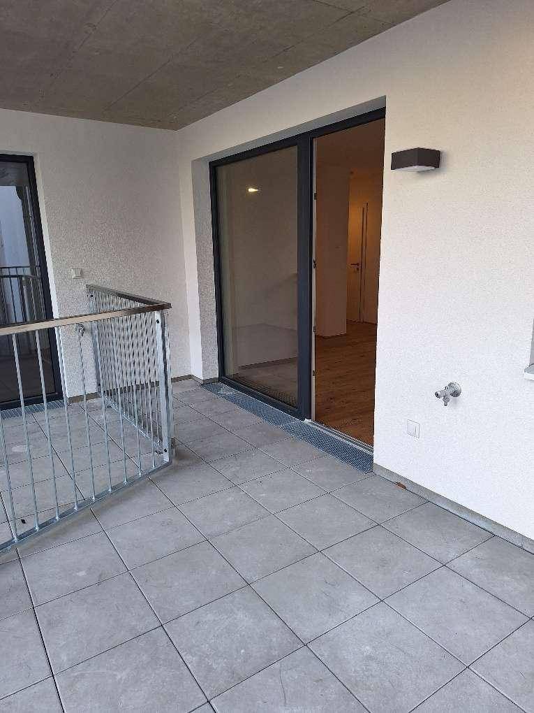 Geräumiger Balkon mit Fliesenboden und Metallgeländer, zugänglich durch eine große Glastür.