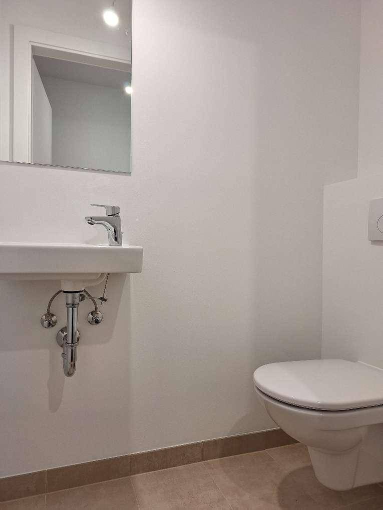 Helles Gäste-WC mit wandhängender Toilette, kleinem Waschbecken und Spiegel in minimalistischem Design.