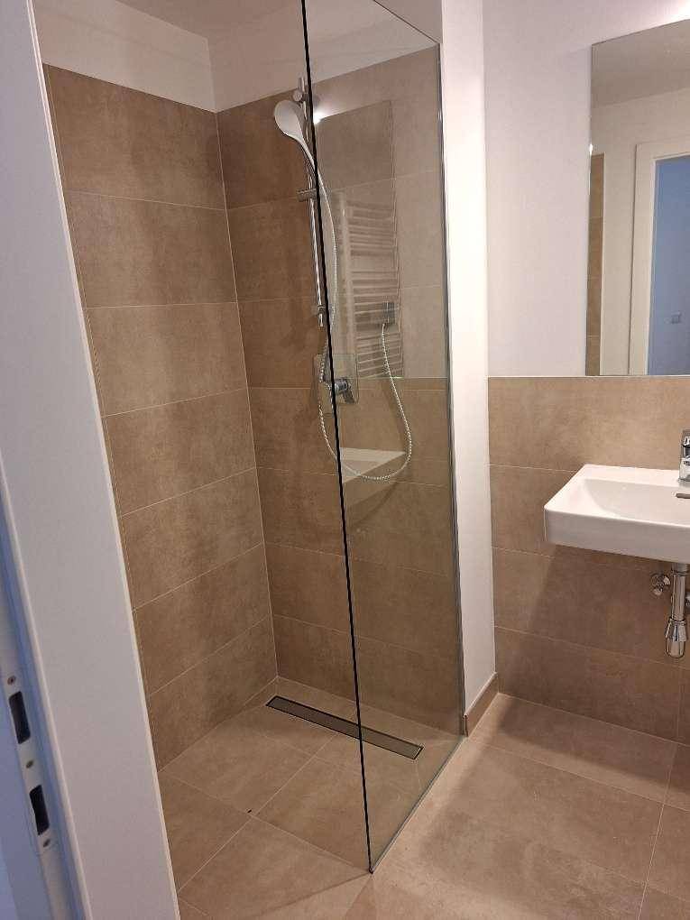 Modernes Badezimmer mit begehbarer Dusche, Glasabtrennung und kleinem Waschbecken mit Spiegel.