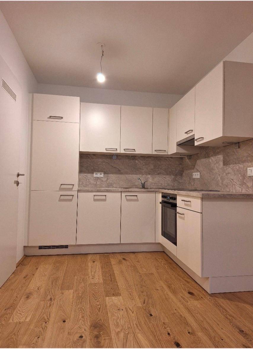 Moderne Einbauküche mit weißen Schränken, integriertem Backofen und hellem Holzfußboden.
