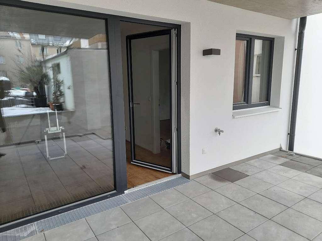 Geflieste Terrasse mit großer Schiebetür, die Zugang zum Innenbereich der Wohnung bietet.