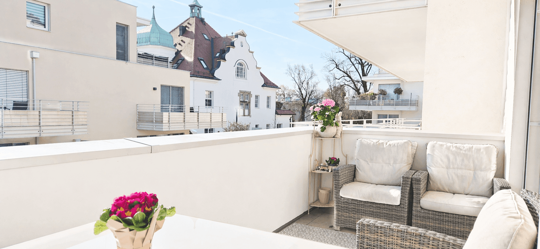Sonniger Balkon mit Rattanmöbeln und Blick auf die umliegenden Gebäude und die Stadt.