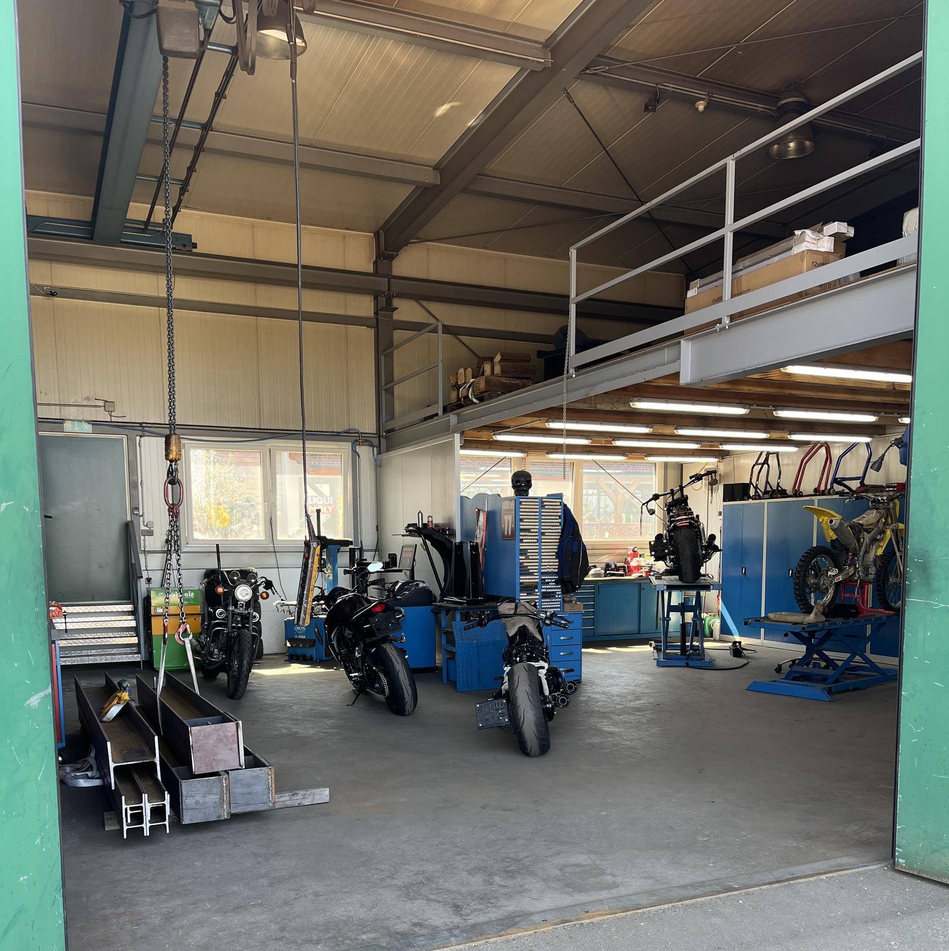 Weitläufige Garage und Werkstatt mit verschiedenen Motorrädern, Werkzeugen und einer erhöhten Lagerfläche.