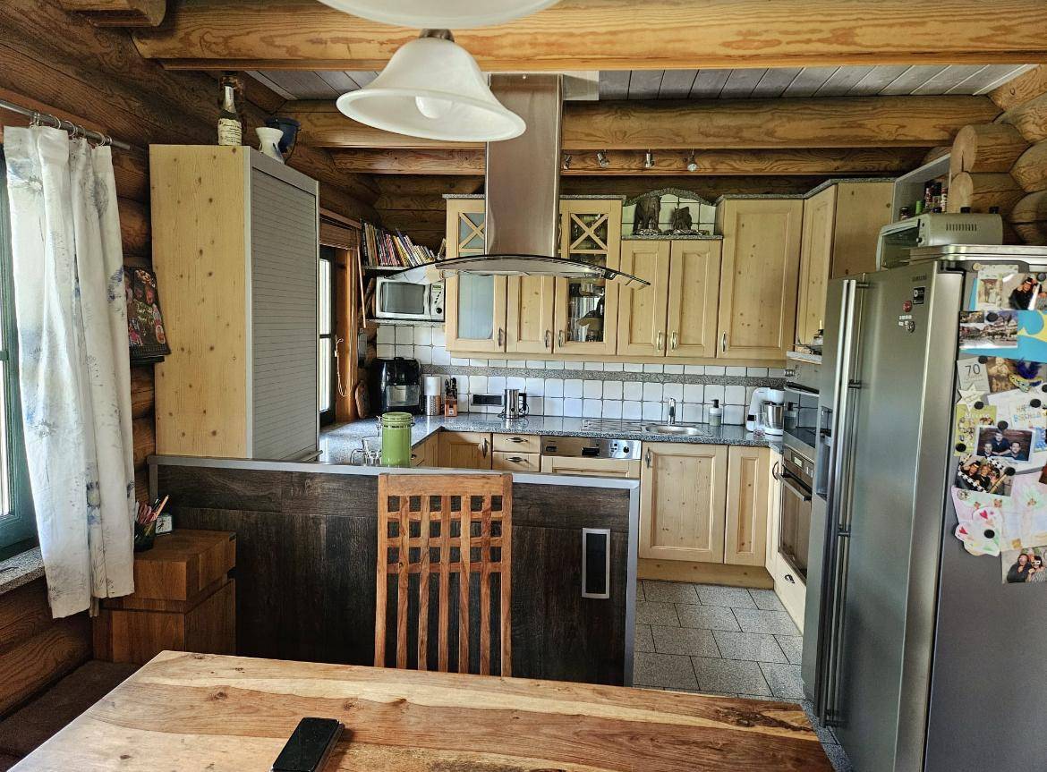 Küche im Blockhaus mit Holzschränken, Arbeitsplatten in Granitoptik, gefliestem Spritzschutz und einem Esstisch.