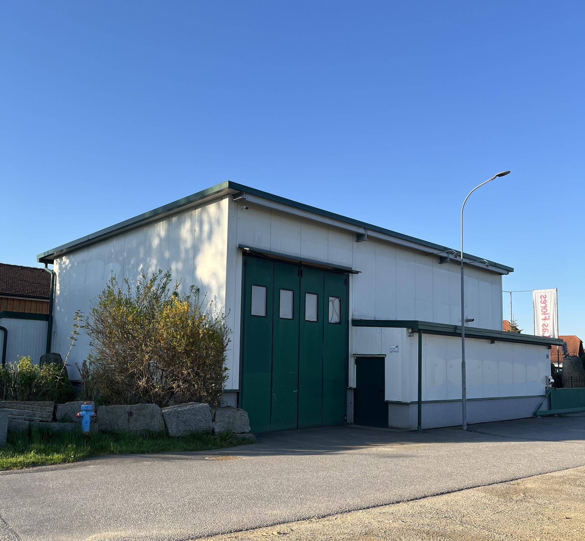 Große weiße Industriehalle mit markanten grünen Toren und einer schlichten Fassadengestaltung.