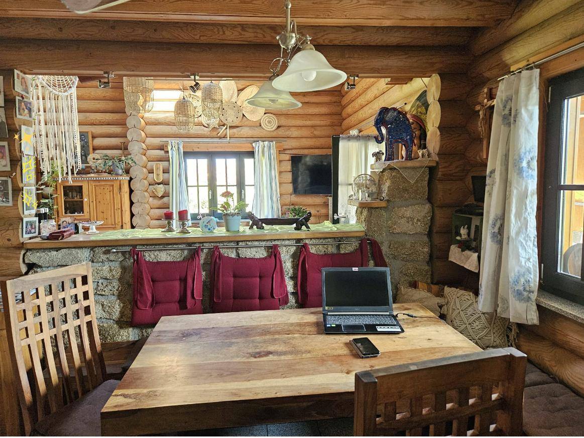 Essbereich im Blockhaus mit großem Holztisch, Holzstammwänden und Blick in den Küchenbereich.