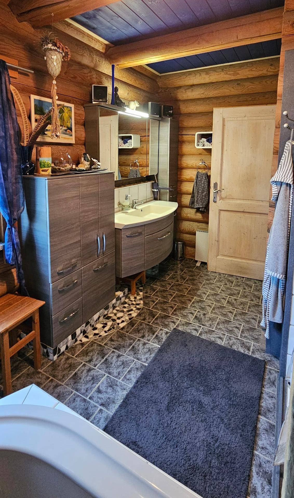 Badezimmer im Blockhaus mit Waschtischunterschrank, Waschbecken, Spiegel und Fliesenboden.