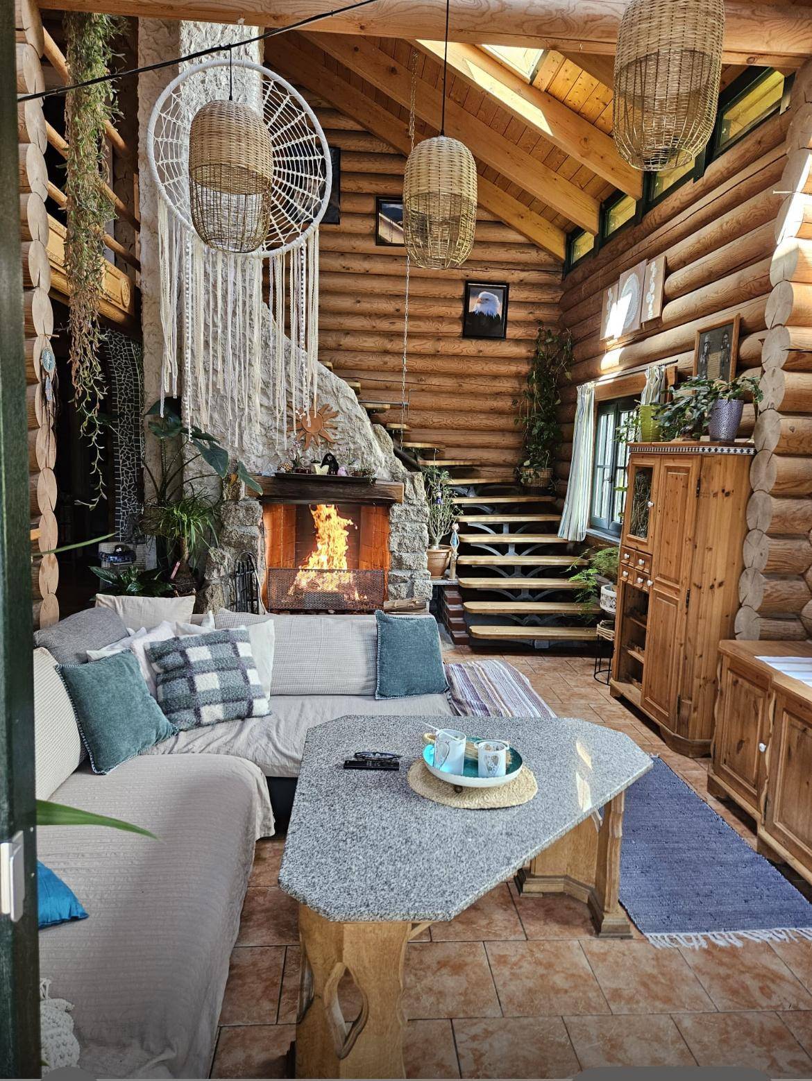 Wohnzimmer im Blockhaus mit Kamin, Sofa, Fliesenboden und einer Holztreppe, die zum Obergeschoss führt.