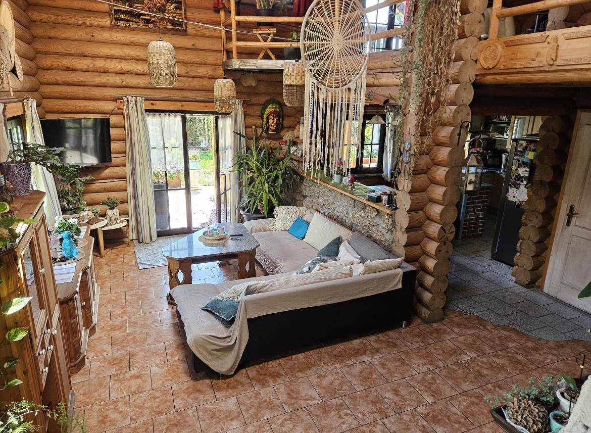 Wohnzimmer im Blockhaus mit Sofa, Fliesenboden und Blick in den Garten durch große Glastüren.