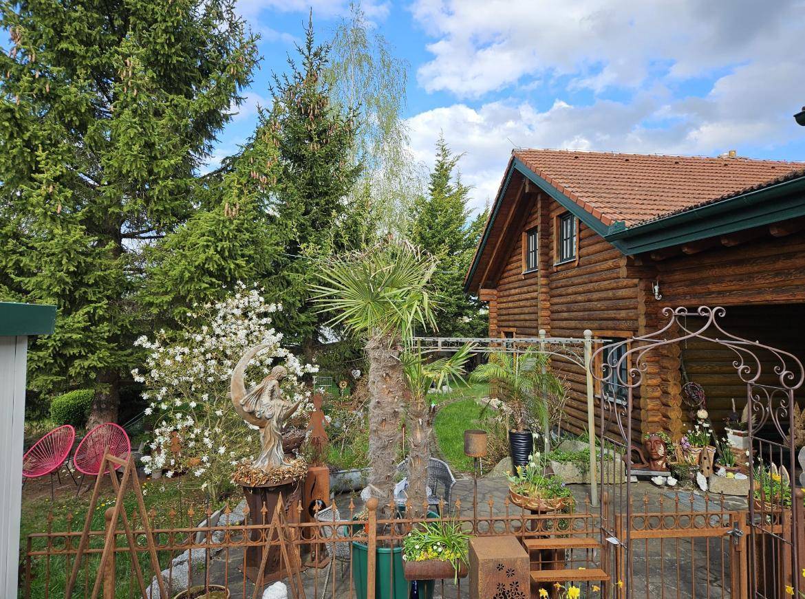 Außenansicht des Blockhauses mit einem liebevoll dekorierten Gartenbereich, verschiedenen Pflanzen und Metallkunstwerken.