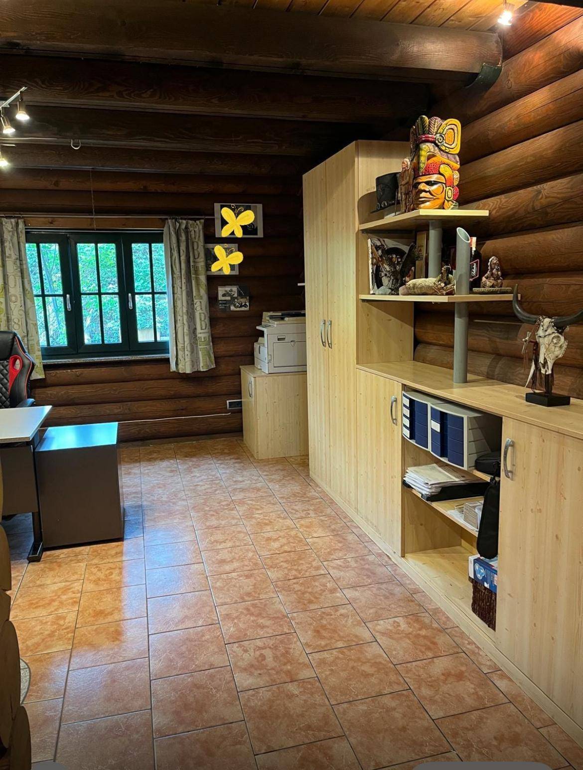 Büro- oder Arbeitszimmer im Blockhaus mit Fliesenboden, Holzschränken und einem Fenster mit Blick ins Grüne.