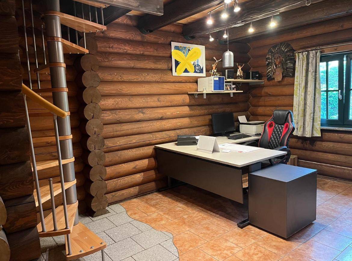 Büro- oder Arbeitszimmer im Blockhaus mit Wendeltreppe, Schreibtisch und Holzstammwänden.