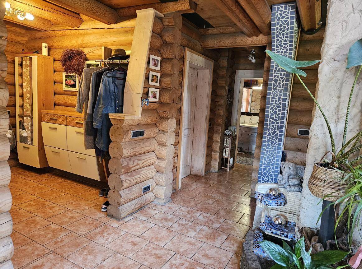 Eingangsbereich oder Flur im Blockhaus mit Holzstammwänden, Fliesenboden und einem Garderobenschrank.