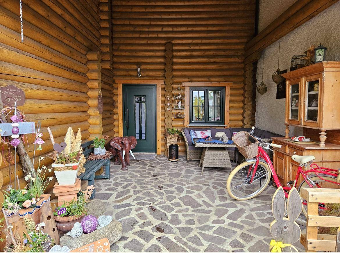 Überdachte Terrasse des Blockhauses mit Steinboden, einer gemütlichen Sitzecke und vielfältigen Dekorationen.