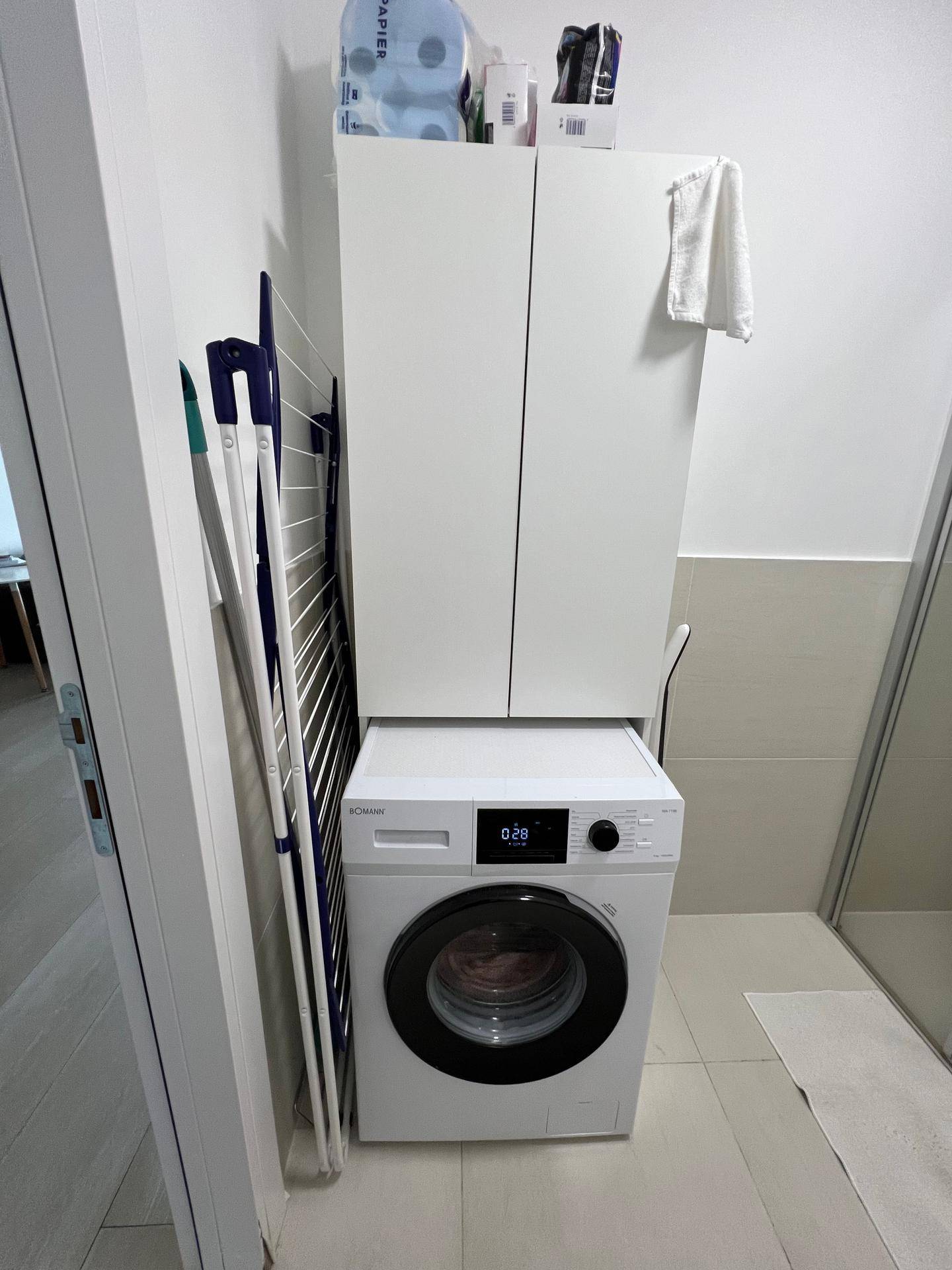 Waschmaschine mit darüberliegendem Schrank und Wäscheständer im Badezimmer.