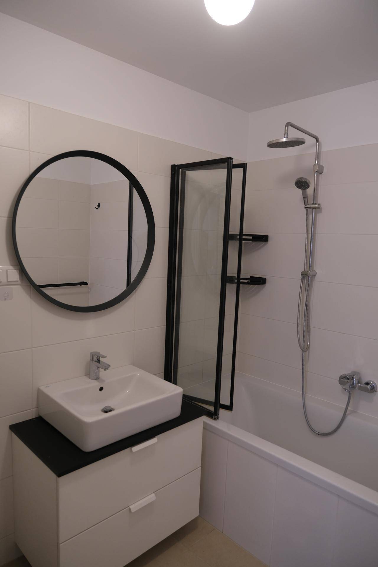 Modernes Badezimmer mit Badewanne, Duschfunktion, Einzelwaschbecken und rundem Spiegel.